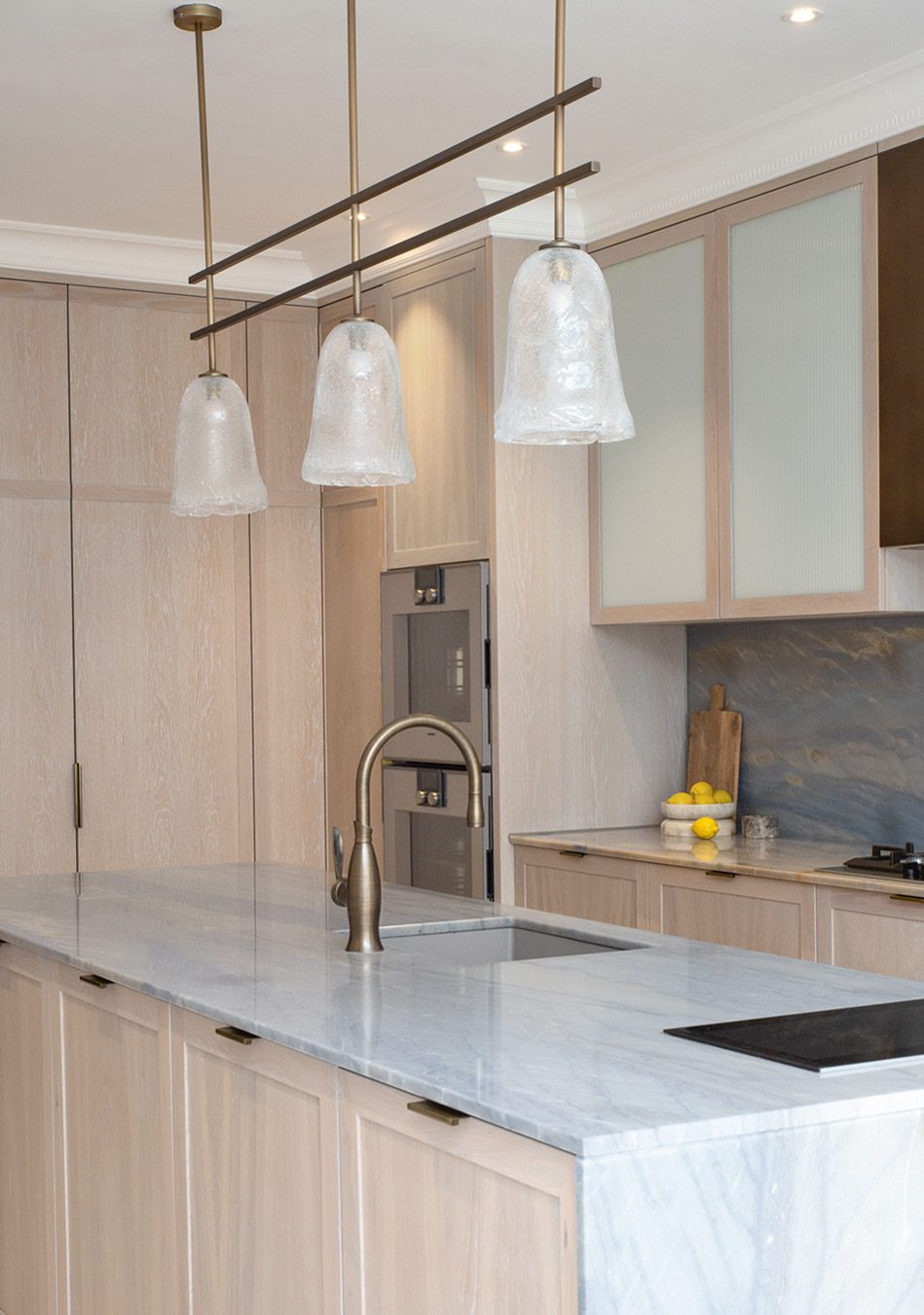 Light oak kitchen with marble island and glass pendants